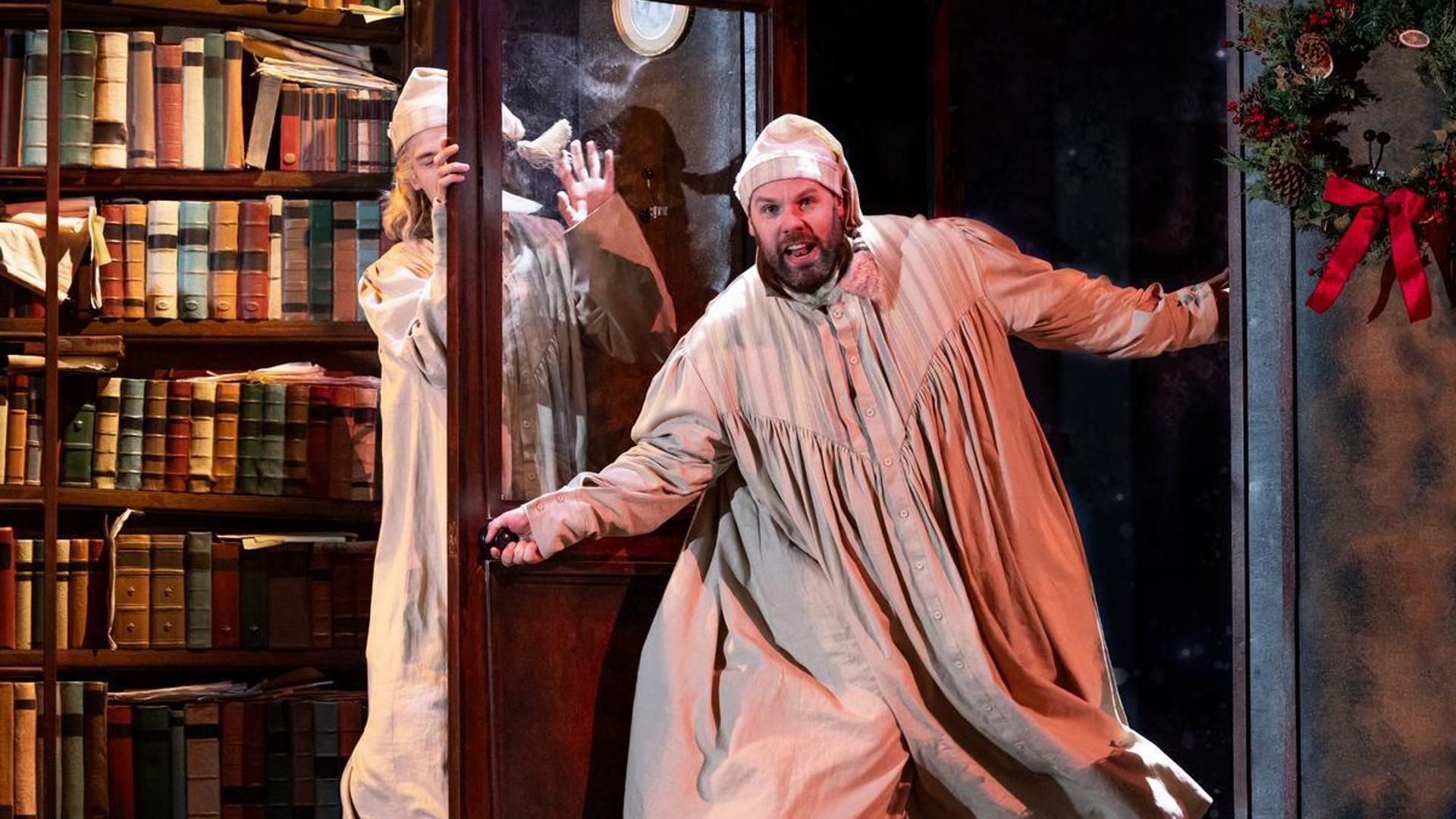 A performer dressed in a nightgown opening a door and hitting another performer with the door.