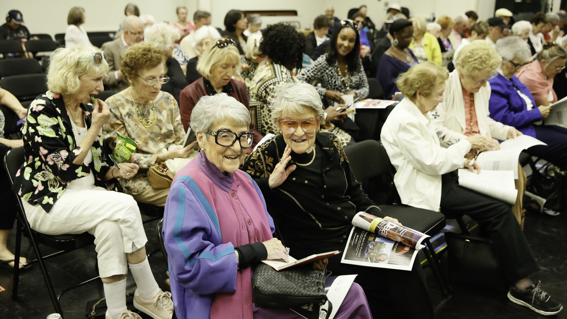 A group of elderly people sit with magazines in their hands. 