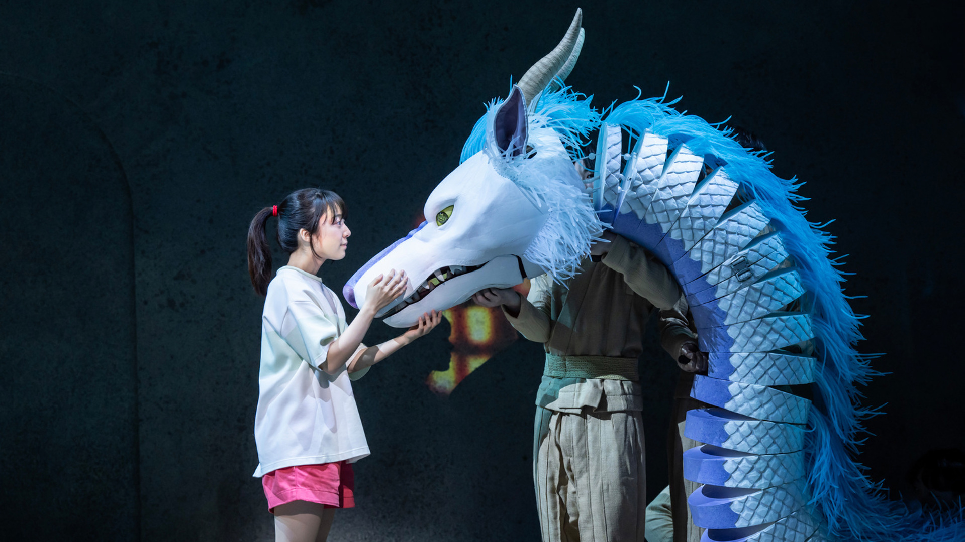 An actor holds on to the face of a blue dragon, looking into its eyes and smiling.