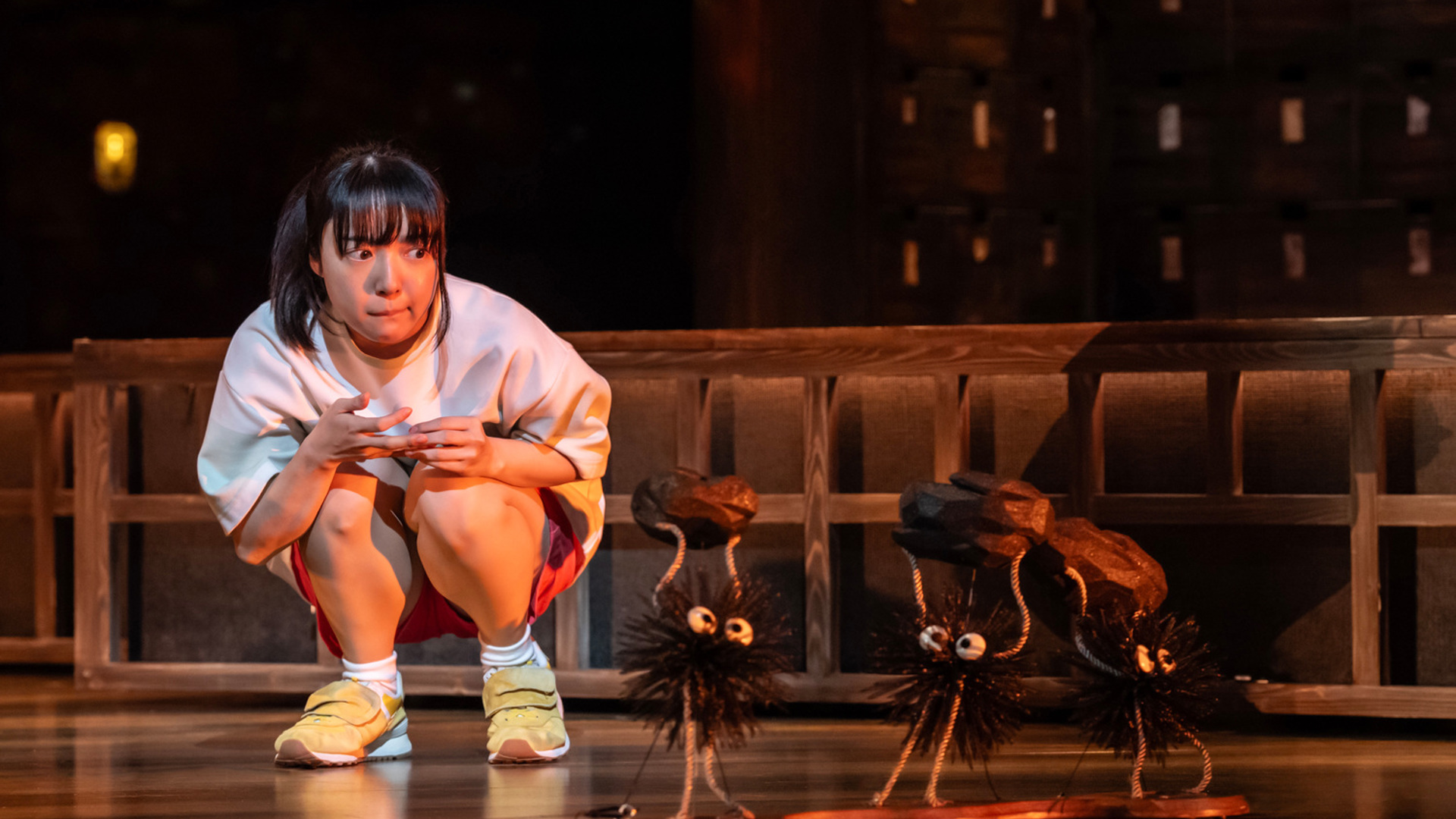 An actor crouches on stage, looking closely at three little black soot creatures, carrying rocks.